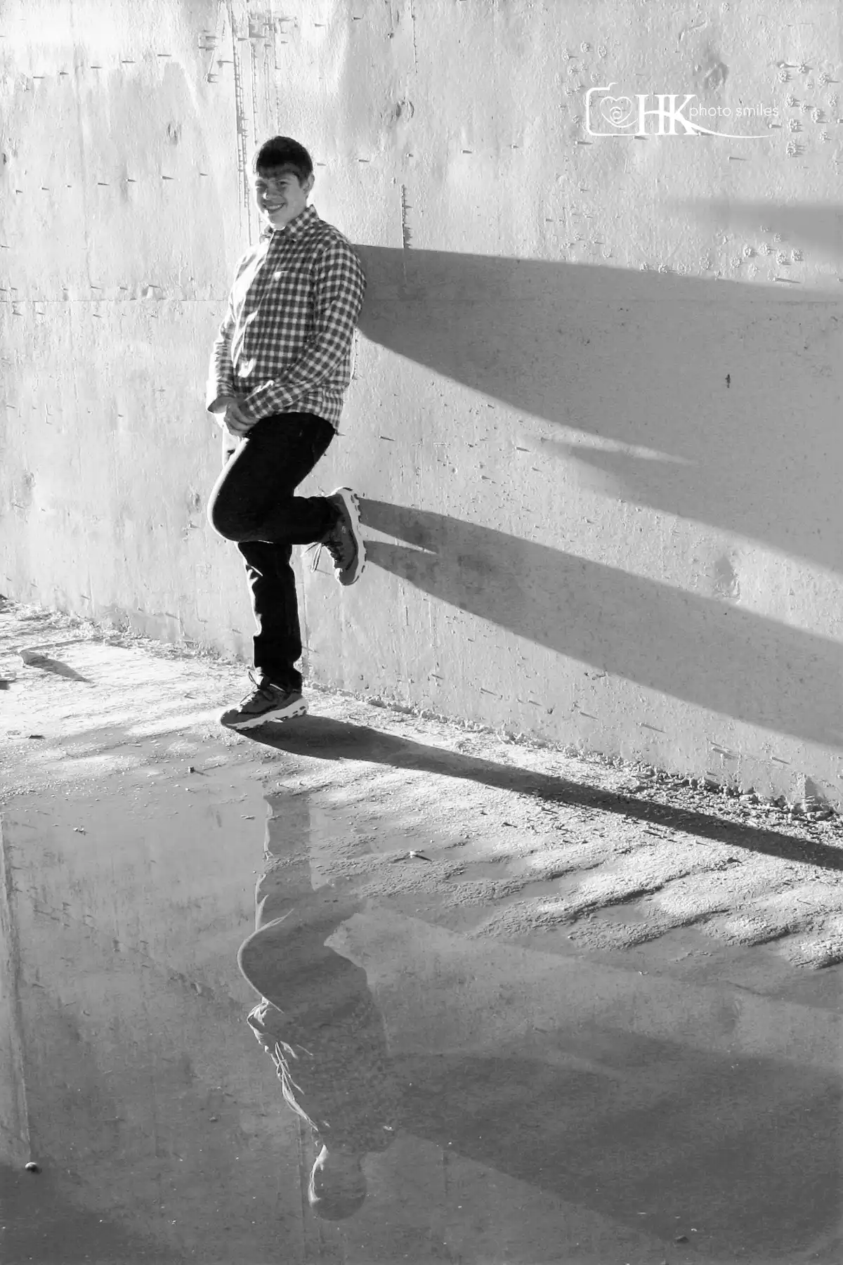 Black and white photograph of older male teenager in tunnel with water and his reflection