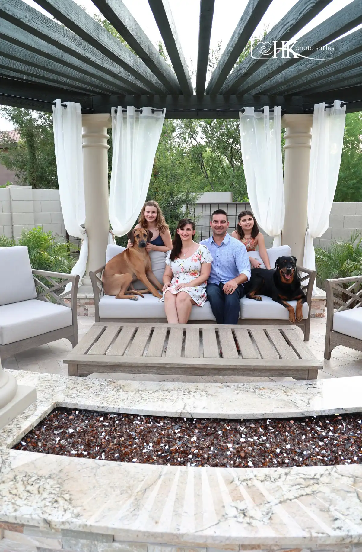 Family portrait of 4 and 2 dogs on family patio with fireplace