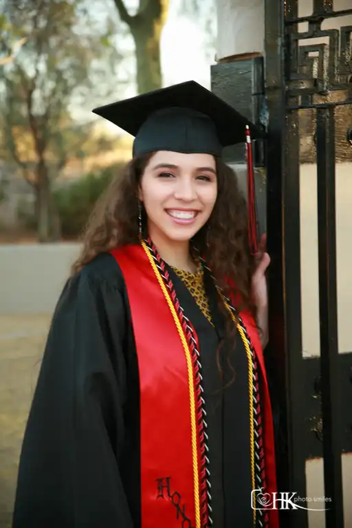 High school grad female wearing cap and gown standing by open gate
