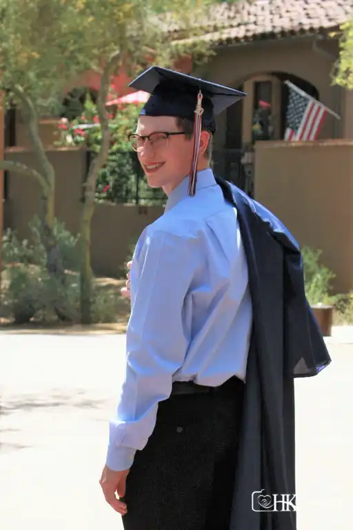 Male high school graduate photo session wearing cap and having gown over shoulder looking back while walking photo