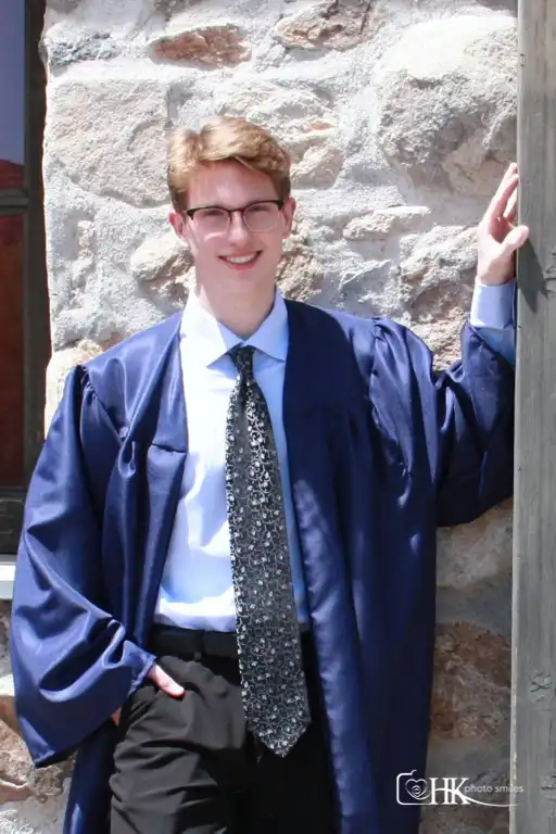 Male high school graduation picture in open gown showing blue dress shirt tie with hand in pocket